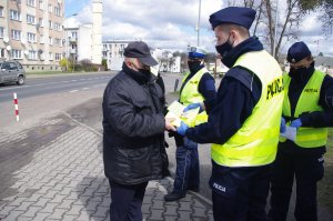 policjant wręcza kamizelkę pieszemu, w tle mundurowi i ulica