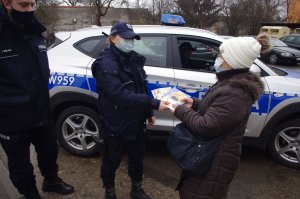 policjanci wręczają seniorce materiały profilaktyczne, w tle radiowóz