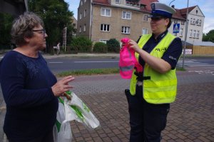 policjantka wręcza kobiecie odblaskowe szelki,  w tle ulica