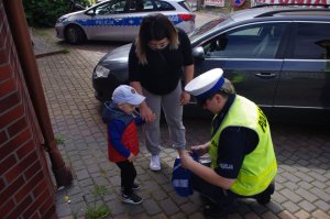 policjantka wręcza dziecku odblaskowe szelki,  w tle radiowóz