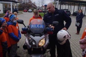 chłopiec na motocyklu obok policjant  w tle teren jednostki