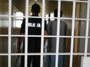 policjant prowadzi zatrzymanego na tle więziennych krat