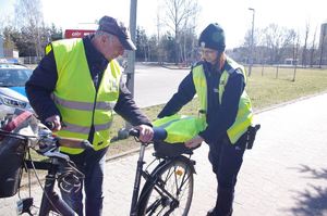 policjantka wręcza odblaski rowerzystom w tle ulica, zabudowania