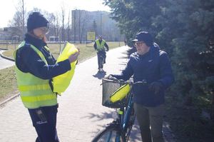 policjantka wręcza odblaski rowerzystom i pieszym w tle zabudowania i droga