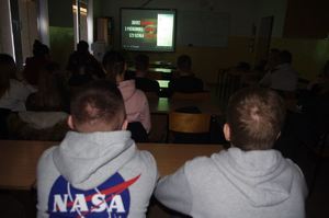 uczniowie oglądają film,  w tle ekran w sali
