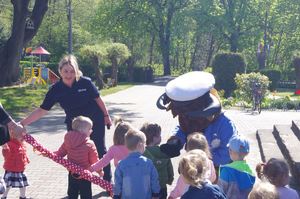 policjantka i policyjna maskotka rozmawia z dziećmi  w tle teren przedszkola