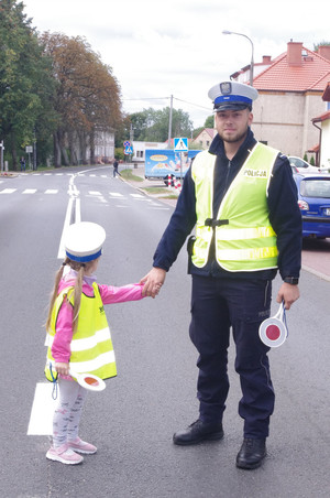 policjanci z przedszkolakami prowadzą działania na drodze w tle ulica i zabudowania