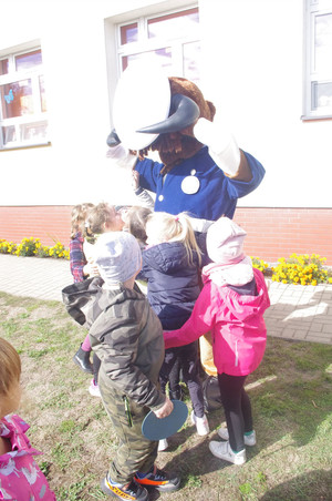 policjantka w towarzystwie maskotki rozmawia z dziećmi w tle teren zewnętrzny przedszkola