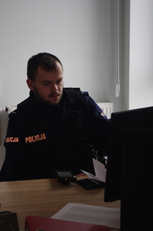 policjant przy komputerze w tle ściana