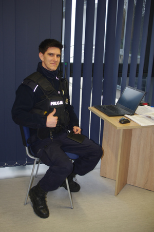policjant siedzi przy biurku w tle roleta okienna