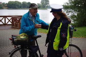 policjantka wręcza rowerzyście odblaskową kamizelkę w tle jezioro
