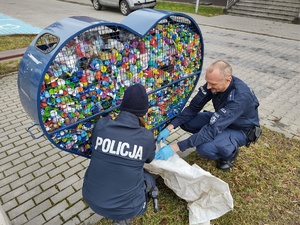 policjanci wybierają nakrętki z metalowego kosza w tle chodnik