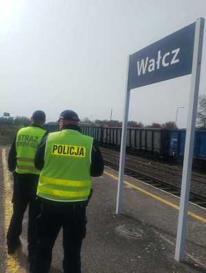 policjant i straż kolei stoją przy torach w tle pociąg towarowy