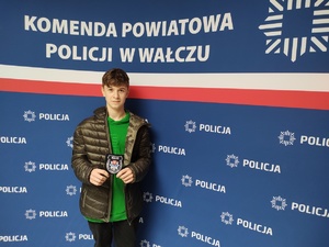 chłopiec stoi na tle ścianki z logo policji w rękach trzyma naszywkę