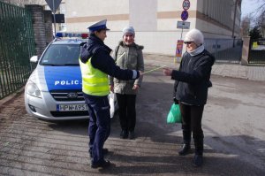 Policjantka wręcza dwóm kobietom odblaski, w tle radiowóz