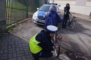 Policjantka zakłada odblaski na szprychy rowerowe, w tle radiowóz