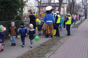Policjanci prowadzą dzieci na spacer, w tle przedszkole