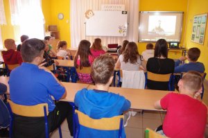 uczniowie oglądają wyświetlany film, w tle ekran a na nim film