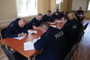 policjanci siedzą przy stole, po obu stronach i rozwiązują test, w tle okna sali