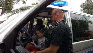 przed drzwiami radiowozu policjant w tle dziecko za kierownicą