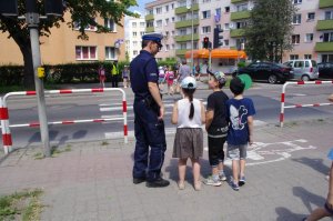 policjant z dziećmi stoi na chodniku, rozmawia w oczekiwaniu na zmiainę światła
