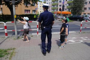 dziewczynka włącza guzik na sygnalizatorze, obok stoi policjant i inne dziecko