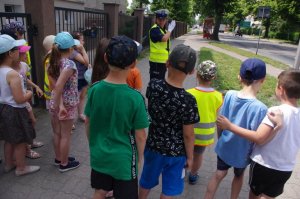 policjantka prezentuje dzieciom  kierowanie ruchem , w tle zabudowania