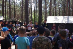 policjanci rozmawiają z wypoczywającymi dziećmi i młodzieżą, w tle namioty, las