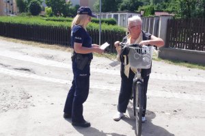 policjantka rozmawia z kobietą, która trzyma rower, w tle zabudowania
