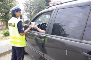 policjantka wręcza kierowcy serce kampanii PZU, w tle kierowca wyciąga rękę przez szybę auta