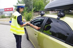 policjantka wręcza serce kampanii PZU kierowcy siedzącemu w aucie,  w tle ulica