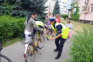 policjantka wręcza odblaski rowerzystom, w tle zabudowania