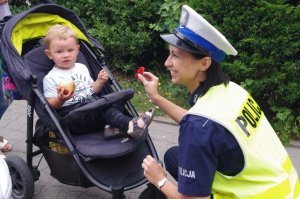policjantka wręcza odblask dziecku w wózku dziecięcym, na tle zieleni