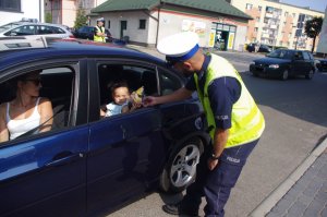 policjant wręcza dziecku będącemu w aucie maskotkę obok matka kierowca