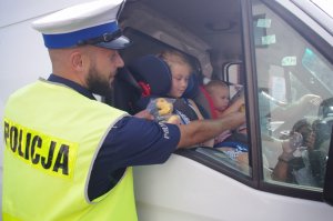 policjant wręcza dzieciom będącym w aucie maskotki