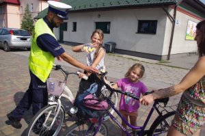 dziewczynki z rowerami otrzymały od policjanta maskotki, w tle miasto