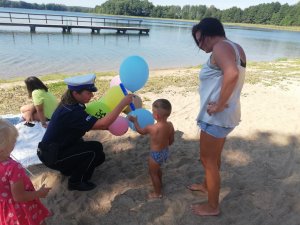policjantka wręcza dzieciom balony, w tle plaża