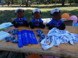 nagrody dla dzieci leżą na stole- pluszowe misie w stroju policjanta, smycze, balony