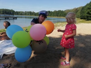policjantka rozdaje dzieciom balony, w tle jezioro