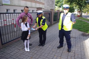 policjant drogówki wręcza dzieciom odblaski w tle szkoła