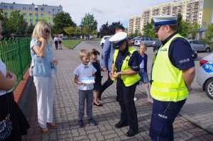 policjant drogówki wręcza dzieciom odblaski w tle ulica