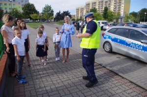 policjant drogówki wręcza dzieciom odblaski w tle ulica i radiowóz