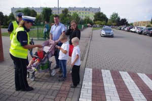 policjant drogówki wręcza dzieciom odblaski w tle przejście dla pieszych