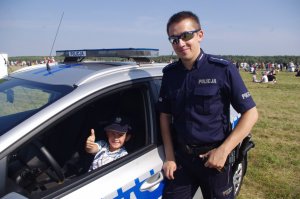 Chłopiec w radiowozie z podniesionym kciukiem, obok policjant