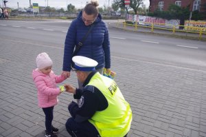 policjant drogówki wręcza dziecku odblask, w tle ulica