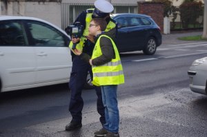 uczeń i policjant sprawdzają prędkość na urządzeniu do pomiaru, w tle ulica