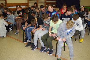 uczniowie siedzą na krzesłach w sali i piszą na kartce,  w tle , drabinki sali gimnastycznej