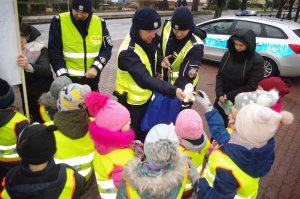 policjanci wręczają dzieciom niespodzianki, w tle ulica