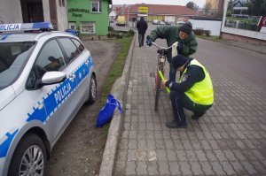 policjant zakłada odblaski na koła rowerowe, w tle zabudowania
