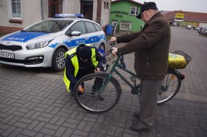 policjant zakłada odblaski na koła roweru. w tle zabudowania